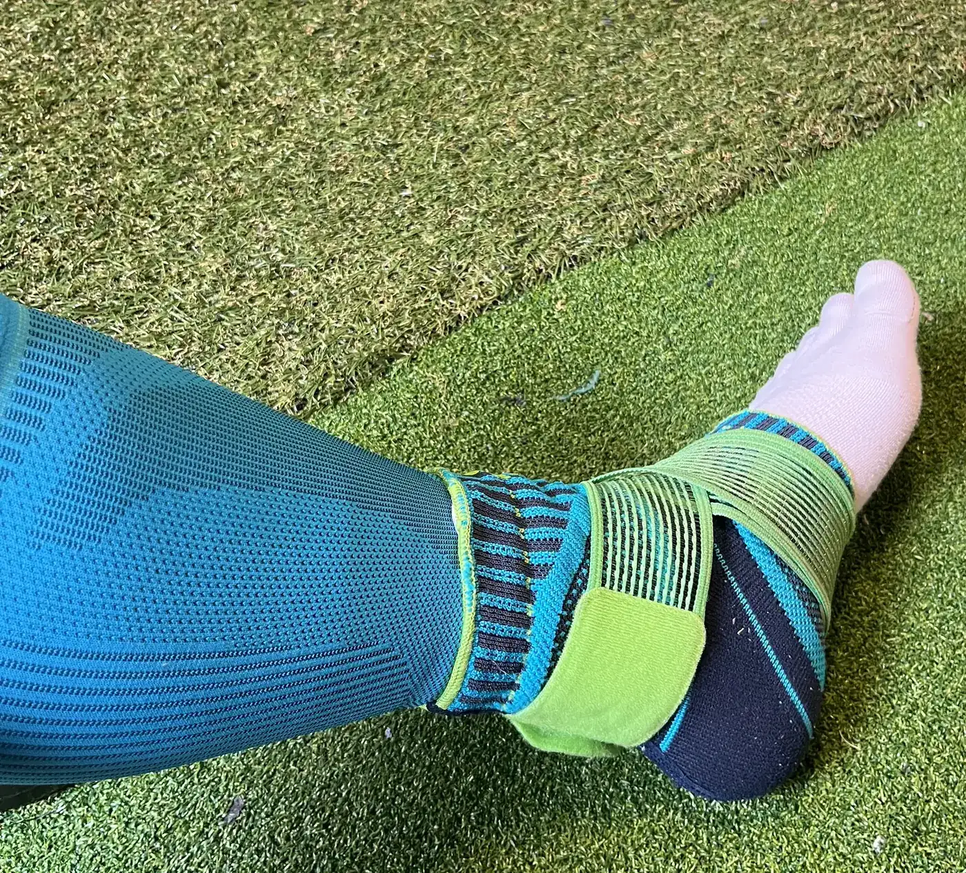 緑のストラップが付いた BAUERFEIND SPORTS ANKLE SUPPORT を装着した左足