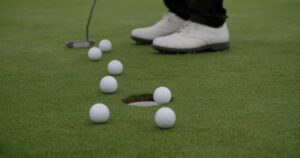 練習グリーンの上で、カップに届かずに止まっている複数のゴルフボール。1球だけがカップの縁にある